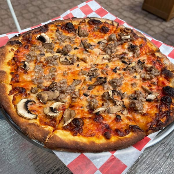 Genaros Restaurant & Pizza's sausage and mushroom pizza, sliced and served on a checkered paper.