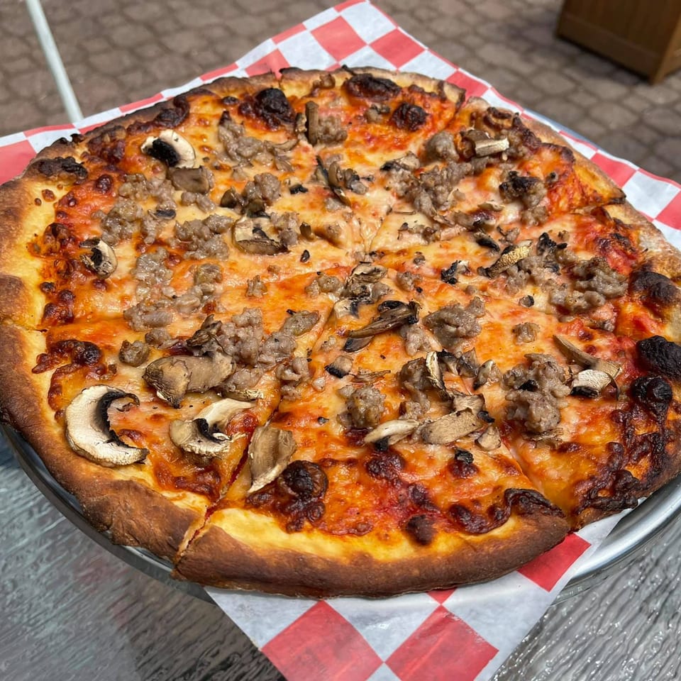 Genaros Restaurant & Pizza's sausage and mushroom pizza, sliced and served on a checkered paper.