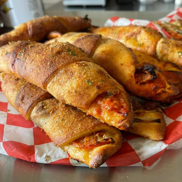Close-up of golden-brown Genaros pizza rolls with melted cheese and sauce on red and white checkered paper.
