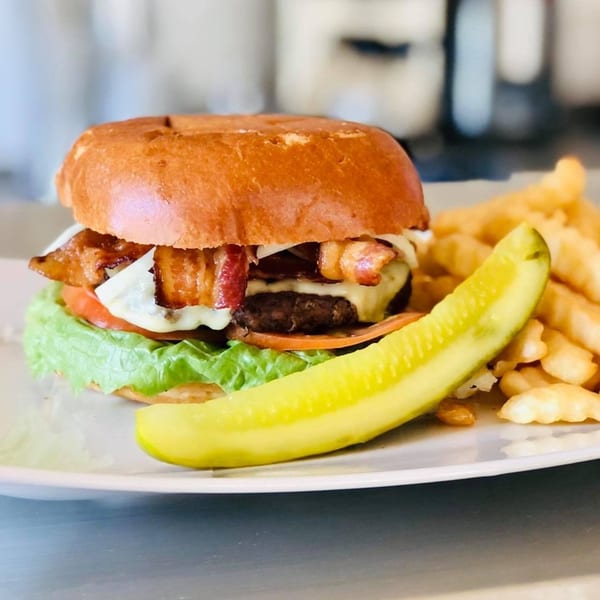 Bacon cheeseburger with lettuce, tomato, and onion, served with crinkle-cut fries and a pickle spear.