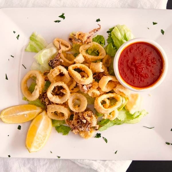 Fried calamari rings and tentacles with lemon wedges, lettuce, and a side of marinara sauce.